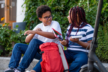 Two schoolkids sitting on the pavement and discussing school issuesの写真素材