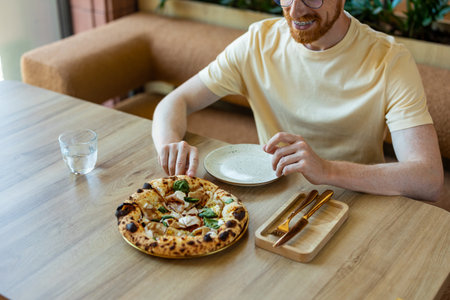 Unrecognizable man enjoying lunch indoors with pizza on plate