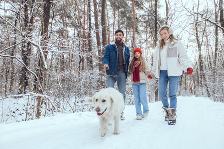 Family having a walk in a snowy forest with a dog and looking happy