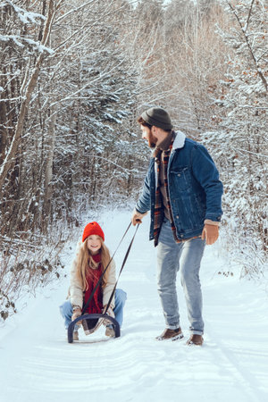 Dad pulling sled with his daughter on it in a winter forest