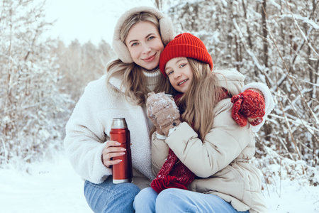 Mom and daughter having tea in a winter forest and looking happy and peaceful