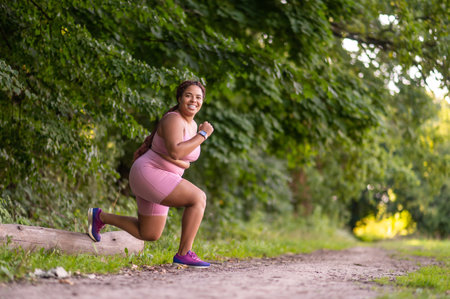 Young african american woman doing lunges in the forest and looking determinedの写真素材