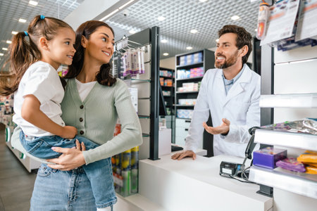 Female customer with daughter communicating with male pharmacist behind counterの写真素材