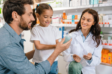Female healthcare worker in white coat consulting male customer with daughter in pharmacyの写真素材