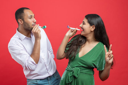 Happy couple celebrating holiday on party blowing in whistle isolated over red backgroundの写真素材