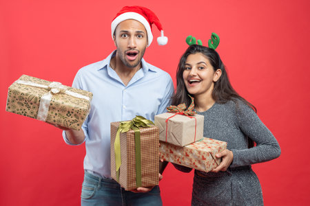Happy couple celebrating Christmas with festive hats and gift boxes congratulating friends at partyの写真素材