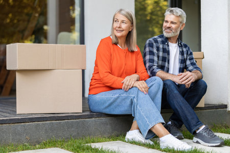 Happy senior couple sitting outside home near moving boxesの写真素材
