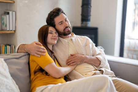 Man and woman sitting on the sofa and feeling romantic while hugging each otherの写真素材