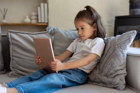 Little girl sitting on sofa using tablet indoorsの写真素材