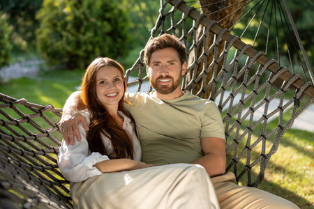 Cute smiling couple enjoying time together while sitting in hammock in the parkの写真素材