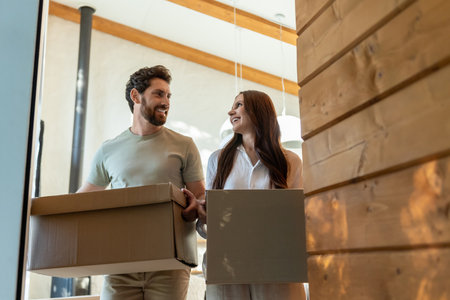 Two people with cardboard boxes entering a house and looking contentedの写真素材