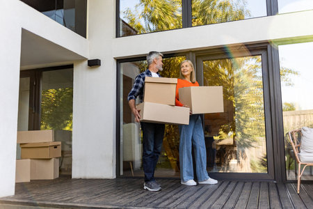 Senior man and woman transporting packed cardboard boxes into new house