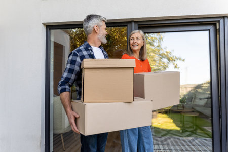 Happy senior couple moving boxes outside residential entrance