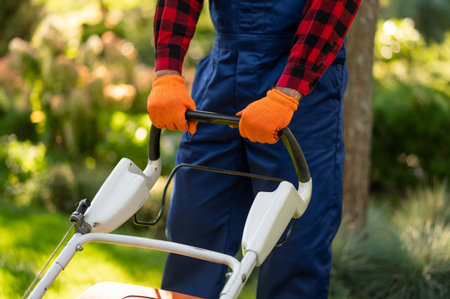 Unrecognizable landscaper mowing lawn in backyard