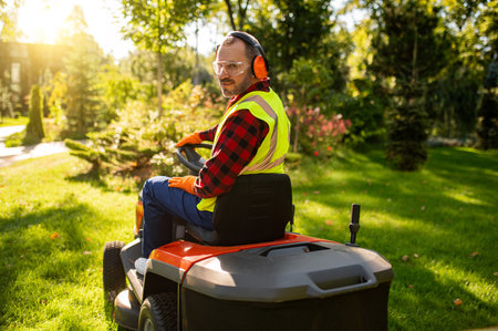 Gardener cutting grass with lawnmower in sunny garden surrounded by green plants