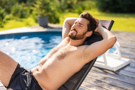 Bearded handsome man lying on a chair near the swimming poolの写真素材