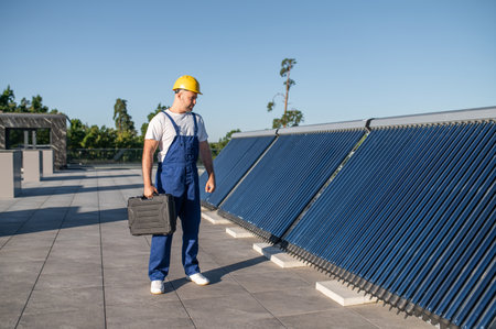 Technician in blue overalls inspecting solar panels on rooftopの写真素材