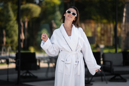 Cute caucasian young woman in white bath robe and sunglasses looking enjoyedの写真素材