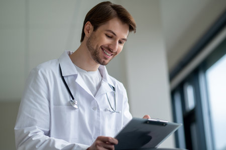Male doctor smiling while holding tablet in clinicの写真素材
