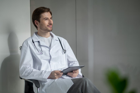 Medical professional sitting with tablet in bright hospitalの写真素材