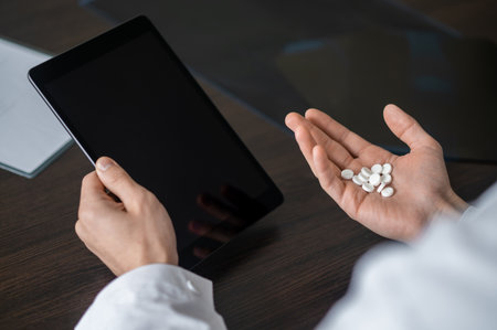 Close-up of hand holding pills and black tablet in clinicの写真素材