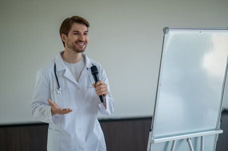 Male doctor standing next to portable white flipchart speaking into microphoneの写真素材