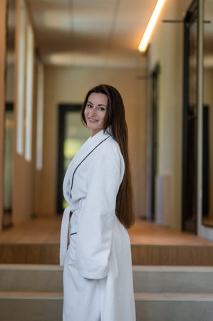 Beautiful young caucasian woman in white bath robe feeling contented and pleased