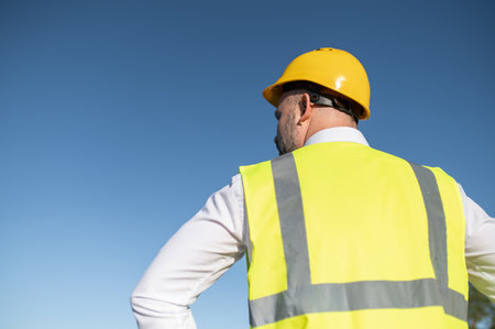 Professional man in safety vest and hard hat looking at horizon