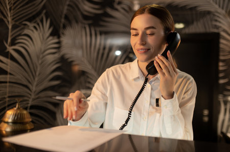 Receptionist talking on the phone while arranging accommodation for the customerの写真素材