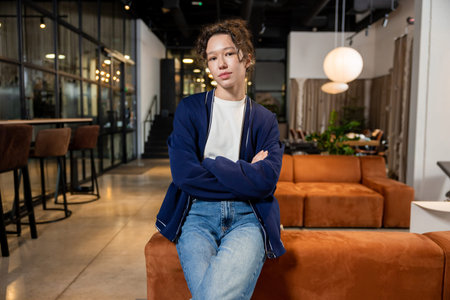 Calm woman seated on orange sofa looking friendly at camera in coworking interior