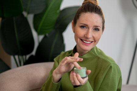 Young smiling woman using moisturizing cream and looking contentedの写真素材