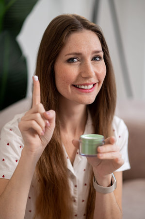 Pretty woman using face cream and looking excitedの写真素材