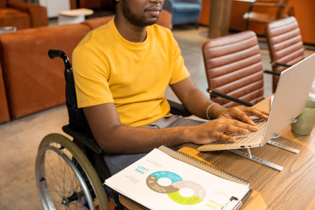 Man in wheelchair working on laptop with online business data in coworking space
