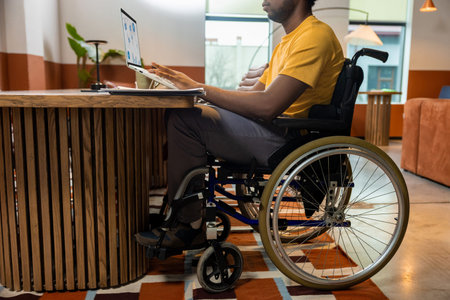Man in wheelchair working on laptop with online business data in coworking space