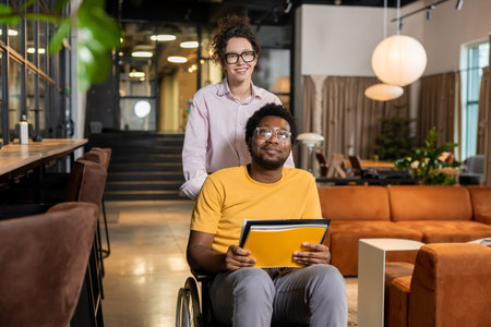 Caucasian woman pushing wheelchair with man holding documents in coworking space