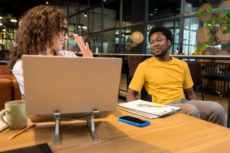 Caucasian woman greeting colleague waving hand using laptop in coworking space