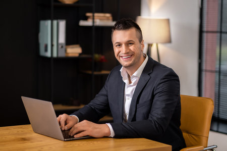 Smiling young businessman in suit browsing laptop