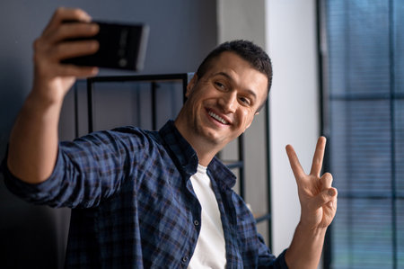 Playful man taking selfie with peace sign standing in office interior