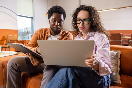 Wavy haired woman and man with laptop and tablet working together