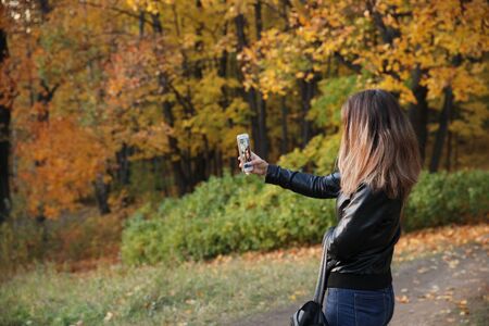 Young girl with a phone in her hand takes a selfie in the autumn Park. Moscow.15.09.2018のeditorial素材