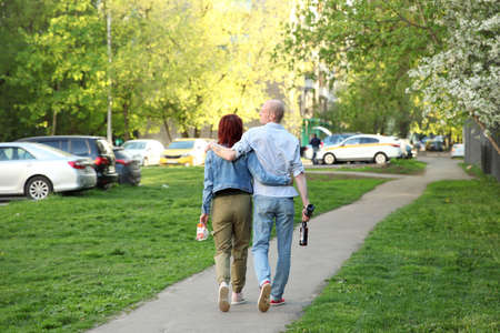 Woman in an embrace with a man who is holding beer bottles walking down the street in the spring....