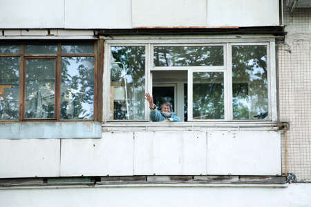An elderly woman in a mask waves as she walks on her balcony. Moscow.11.05.2020のeditorial素材