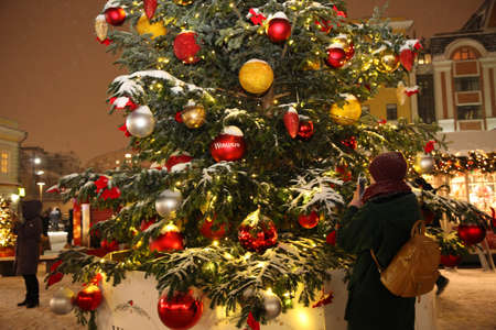 Woman is photographed against the background of a large Christmas tree at the city's new year's fair in the evening. Moscow. 24.12.2018のeditorial素材