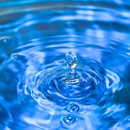 Clean blue drop of water splashing in clear water. Abstract blue background