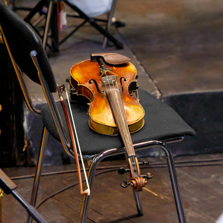 Image of an old violin and bow lying on a chair in a theaterの写真素材