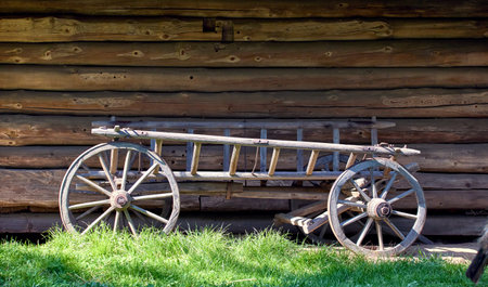 Image of an old wooden cart with large wheels standing near a wooden Ukrainian house in the yard