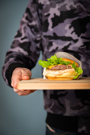 Man holding a hamburger on a wooden board. Close-up.の写真素材