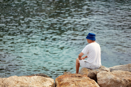 Senior man sitting on the rocks by the sea and looking at the seaのeditorial素材