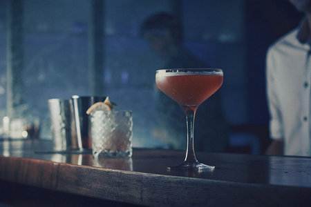 Cocktail on bar counter with bartender in the background at night