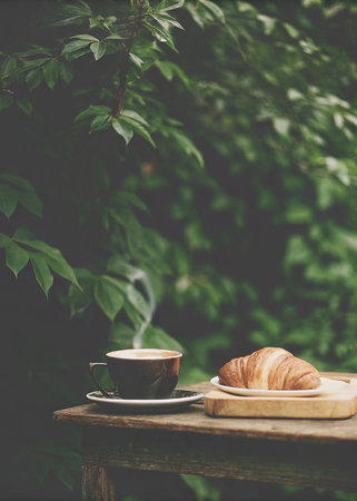 Coffee cup and croissant on wooden table in gardenの写真素材